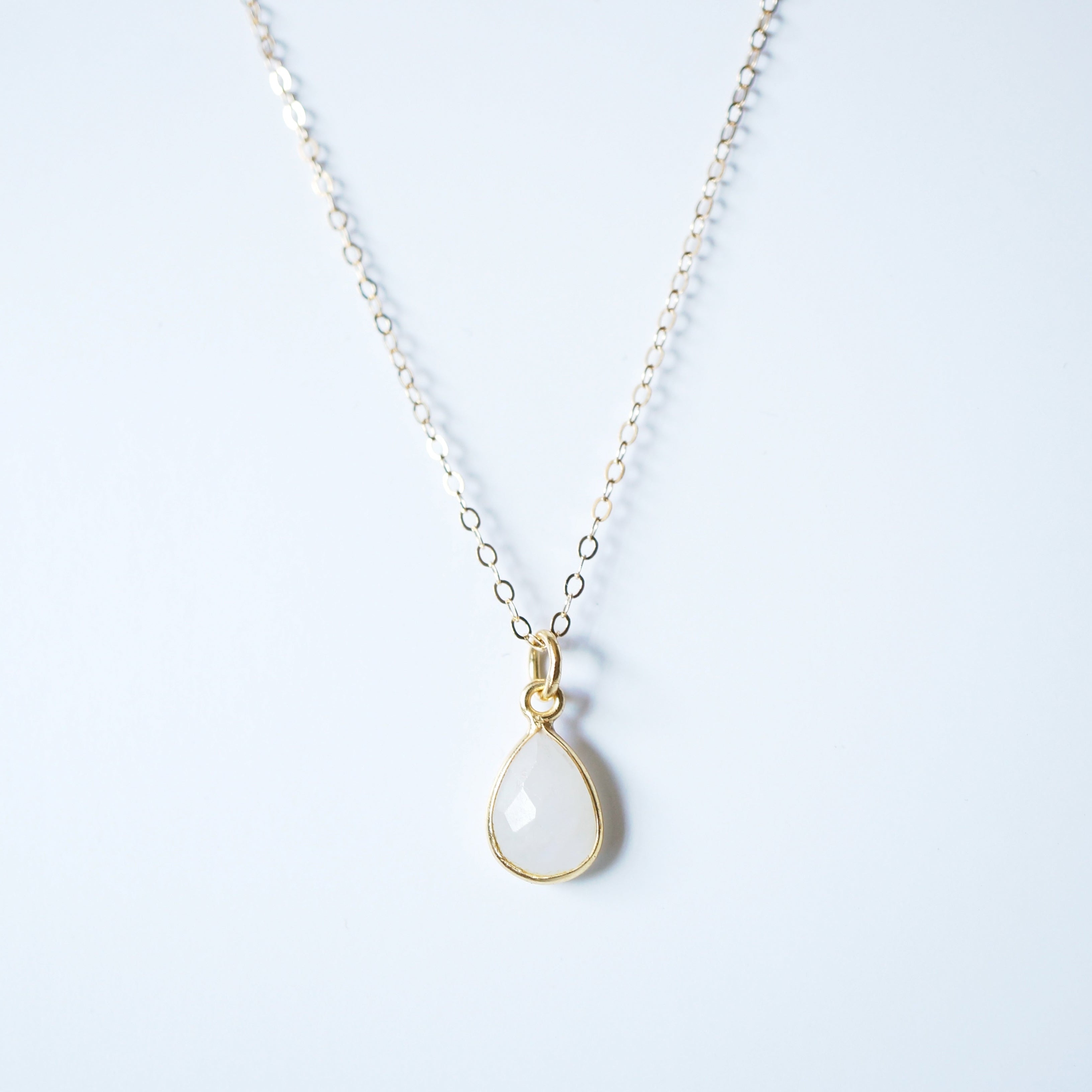 Gold necklace with a teardrop-shaped pendant on a light blue background