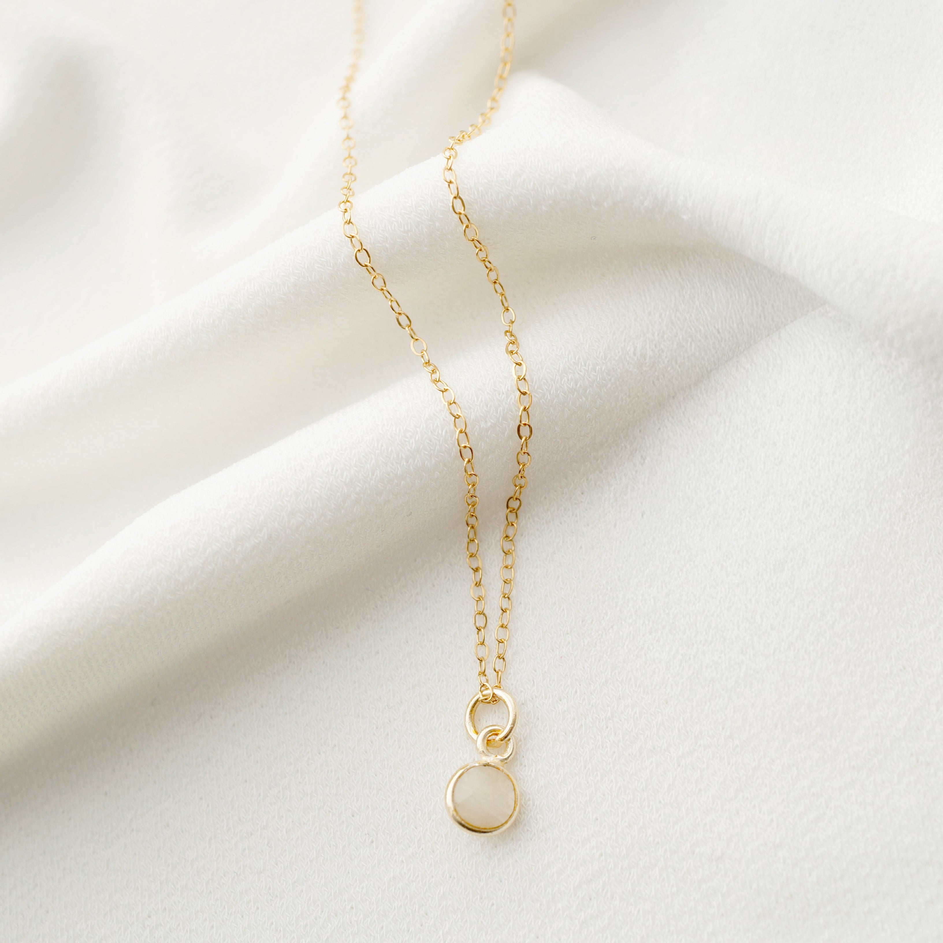 Gold necklace with a small pendant on a white fabric background