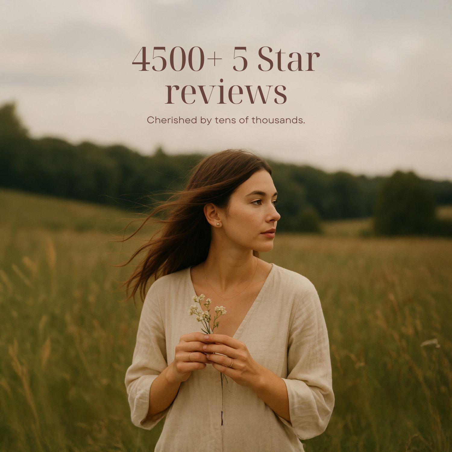A woman stands in a field of tall grass, holding a small bouquet of flowers, with a cloudy sky in the background.